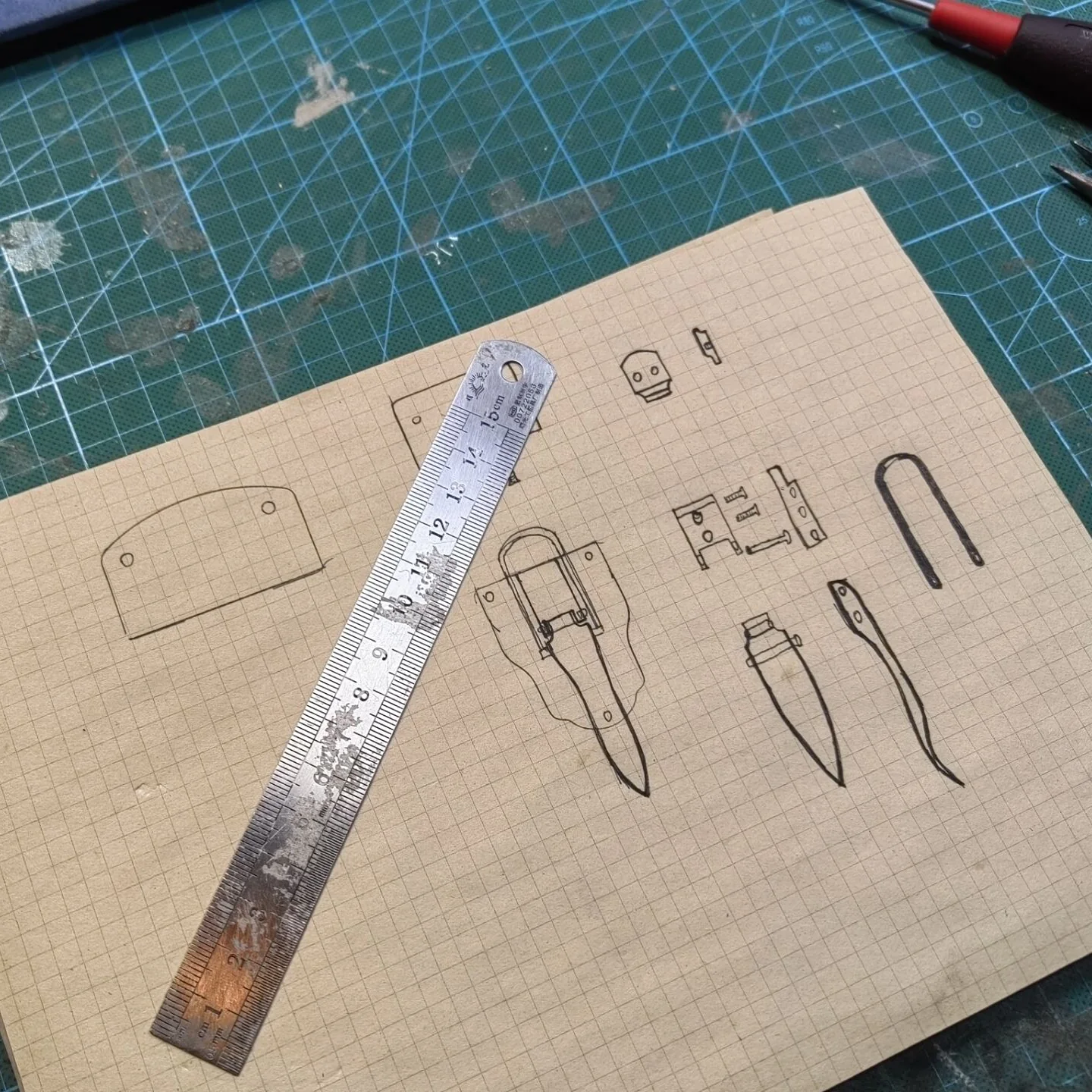 Hand-drawn case fittings beside a ruler on a workshop cutting mat